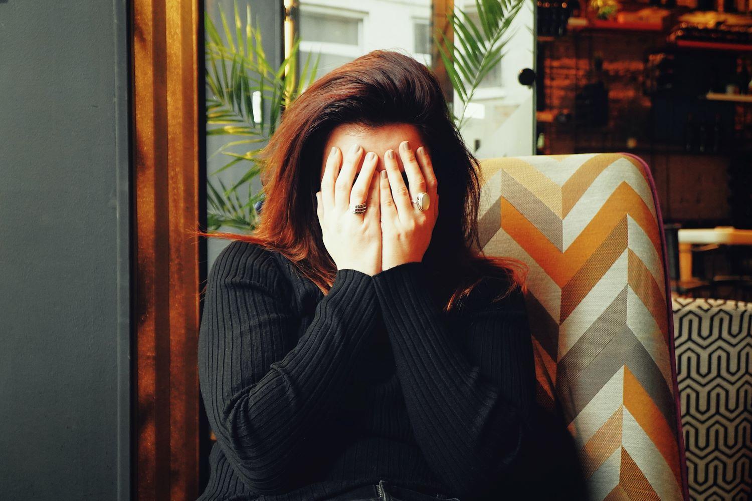 Entrepreneur with hands over her face feeling shy and not being visible